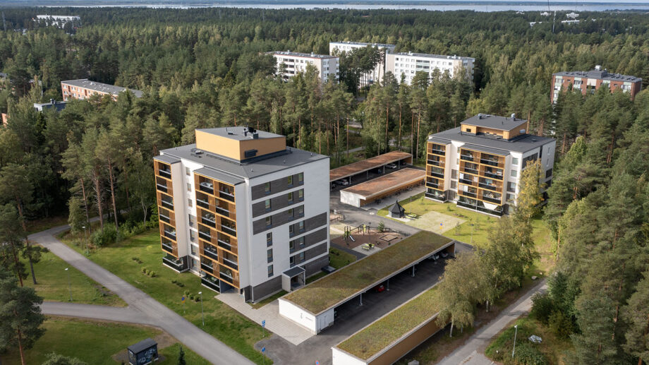 Ilmakuva useammasta kerrostalosta metsäisessä ympäristössä, taustalla merenrantaa.