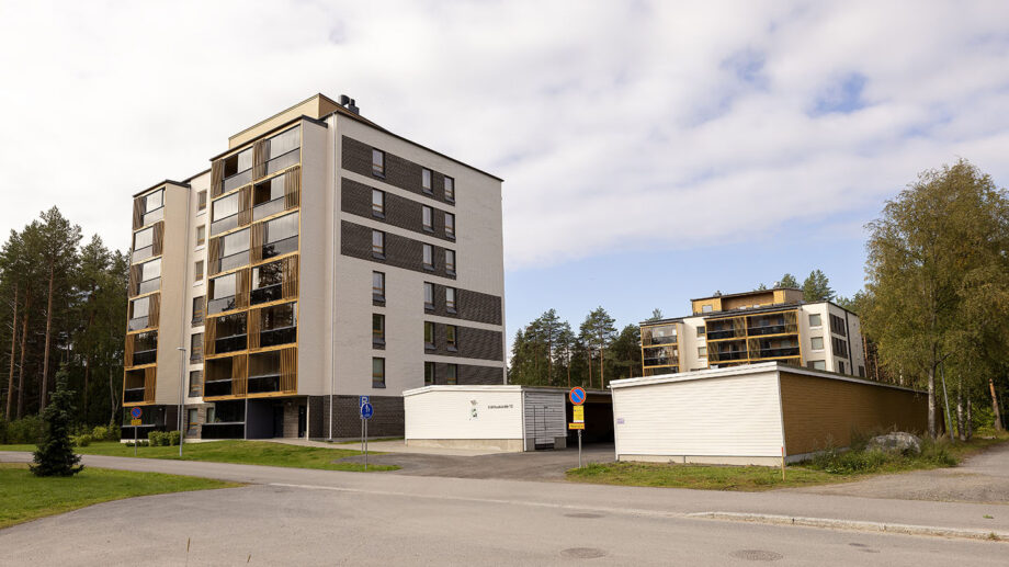 Kerrostalon sivujulkisivu ja autokatos, taustalla toinen asuinrakennus.