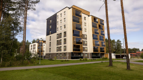 Moderni kuusikerroksinen asuinkerrostalo, vaalea ja tumma julkisivu, nurmikko etualalla.