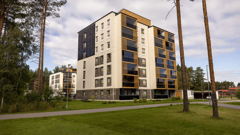 Moderni kuusikerroksinen asuinkerrostalo, vaalea ja tumma julkisivu, nurmikko etualalla.