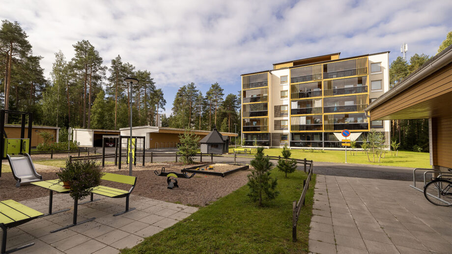 Asuinkerrostalon piha-alue, istutuksia, penkkejä ja kivetyksiä, taustalla rakennus.