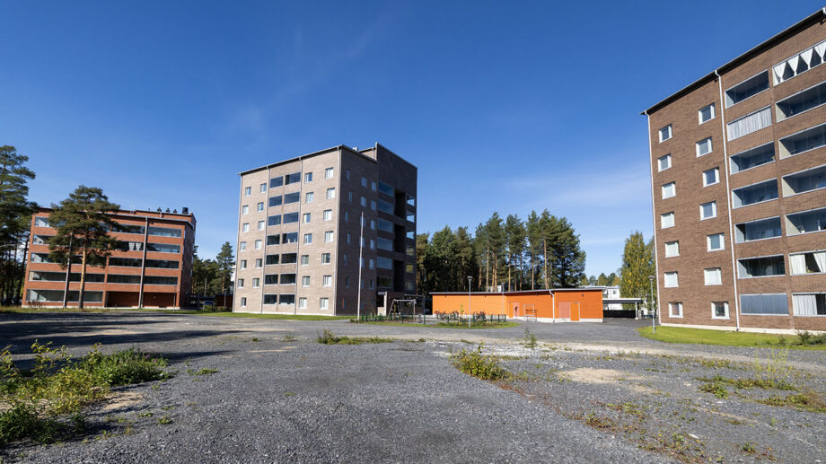 Kerrostaloalue, jossa harmaa ja punatiilinen rakennus sekä pysäköintialue etualalla.