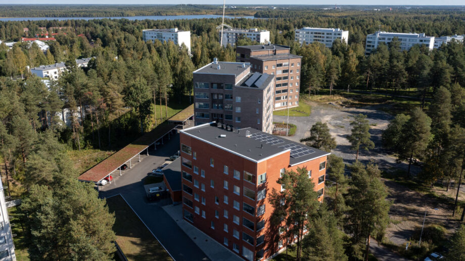 Ilmakuva punatiilisestä ja harmaasävyisestä kerrostalosta, taustalla merenrantaa.