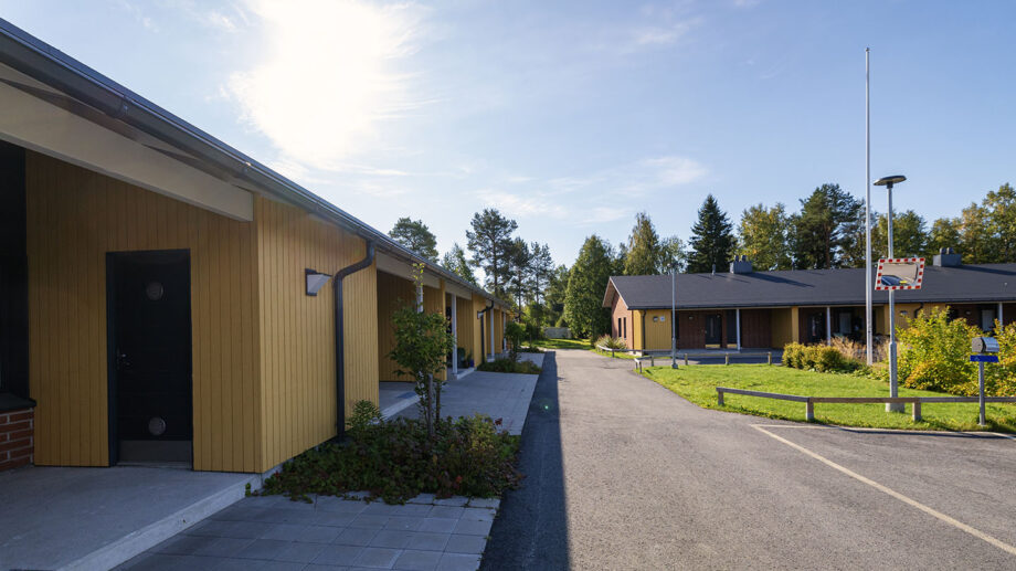 Vaaleankeltainen yksikerroksinen rivitalo, asfaltoitu sisäänajotie etualalla.