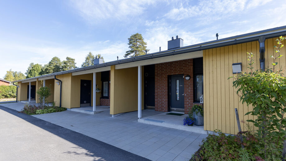 Vaaleankeltainen rivitalo, katettu sisäänkäynti ja pihapolku.