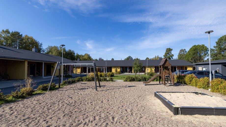 Leikkipiha, hiekkakenttä ja keinuja rivitalojen pihassa.