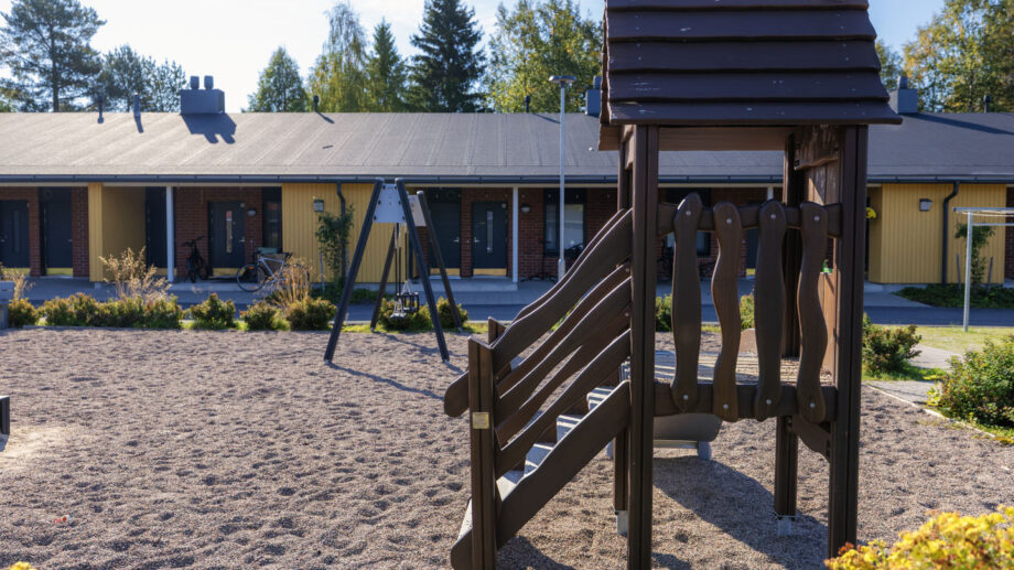 Leikkipiha, puiset kiipeilytelineet ja rivitalot taustalla.