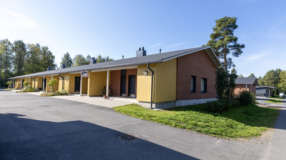 Punatiilinen ja keltainen yksikerroksinen rivitalo, aurinkoinen piha.