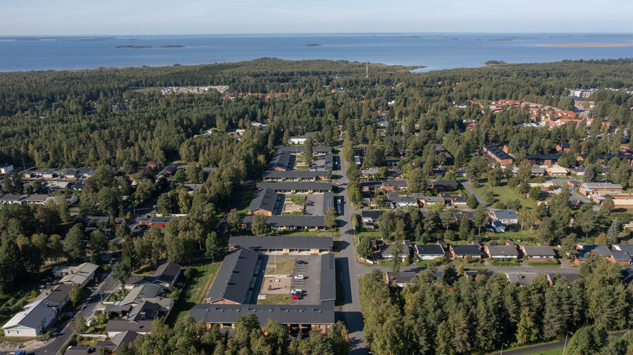 Ilmakuva rivitaloalueesta meren rannalla, ympärillä metsää ja rantaviivaa.
