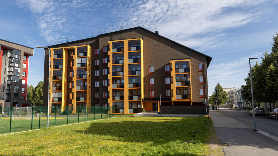 Moderni kerrostalo, punaisia ja keltaisia parvekkeita, edessä nurmikko ja kävelytie.