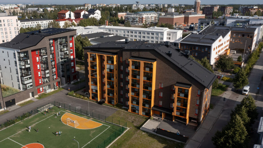 Ilmakuva kerrostalosta, jonka edustalla koripallokenttä ja viheralue, ympärillä kaupunkirakennuksia.