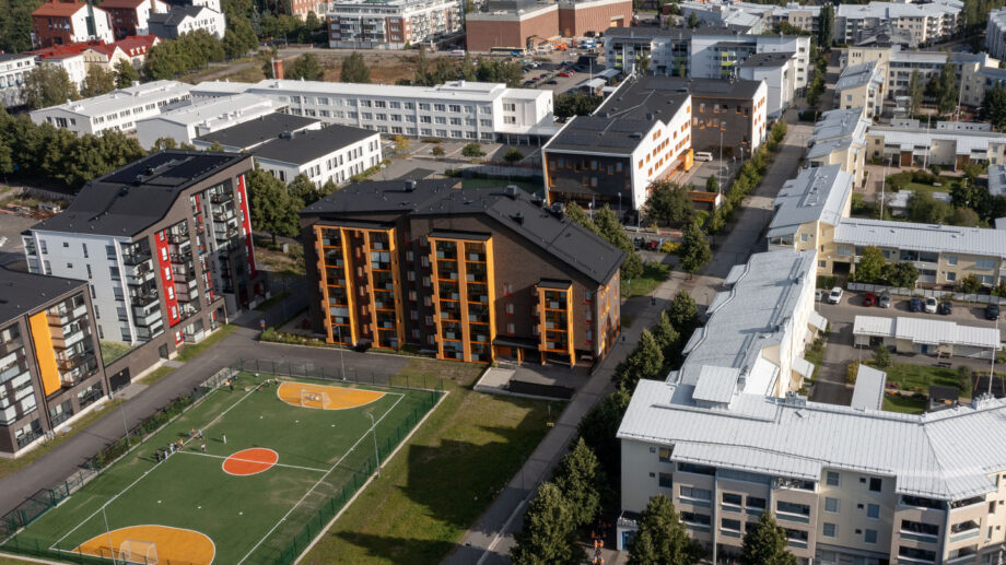 Ilmakuva kaupunkikorttelista, keskellä oranssi-punasävyinen kerrostalo ja viheralue.