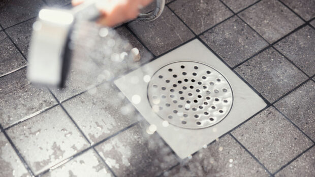 Suihkulla valutetaan vettä lattiakaivoon kylpyhuoneessa, jossa on laattalattia.
