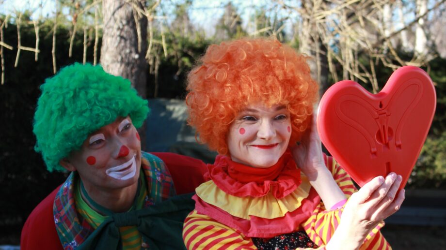 Kuvassa kaksi pelleä katsooa itseään sydämen muotoisesta peilistä. Taustalla puita sekä kuusiaita.