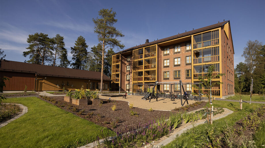 Asuinkerrostalo, puu- ja tiilipintainen julkisivu, istutuksia ja istuma-alue pihassa.