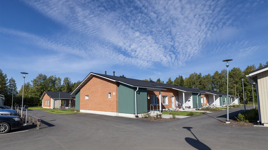 Kulmanäkymä yksikerroksisesta rivitalosta, tiiliverhous ja asfaltoitu piha-alue.