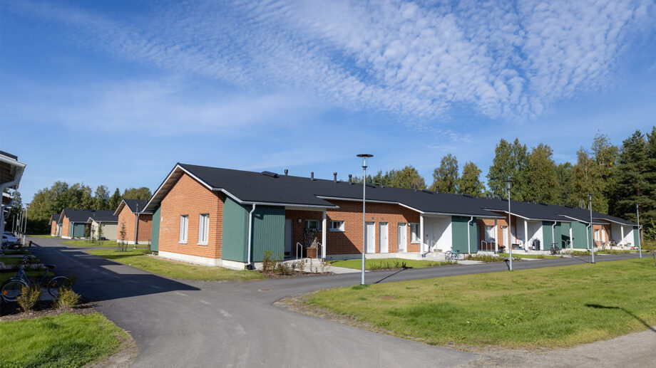 Rivitalo, jossa punatiilinen ja vihreäsävyinen julkisivu, piha ja kulkuväylä edessä.