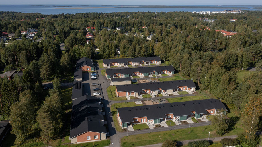 Ilmakuva rivitaloalueesta metsän laidalla, taustalla näkyy merenrantaa.