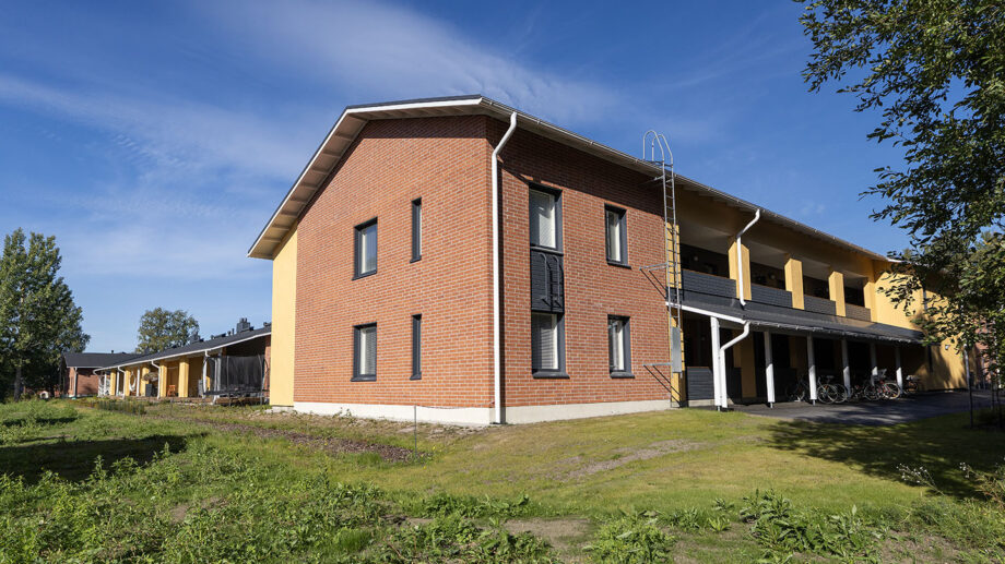 Kaksikerroksinen punatiilinen asuinrakennus, nurmipiha etualalla.