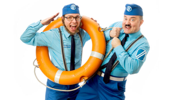 Kaksi iloista miestä sinisissä asuissa poseeraa. Toisella on pelastusrengas kaulassaan, ja molemmat hymyilevät leveästi kameralle.