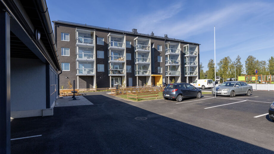 Nelikerroksinen asuinkerrostalo, pysäköintialue ja sisäänkäynti näkyvissä.
