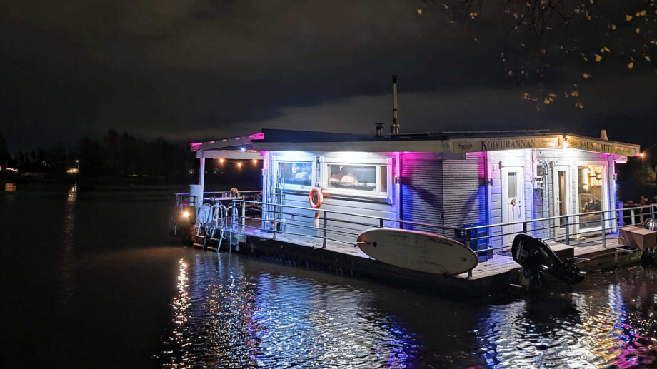 Valaistu saunalautta vedellä pimeässä illassa, ympärillä heijastuksia ja syksyisiä puita.